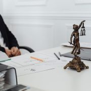 Mesa de trabalho jurídico com documentos, laptop e uma estátua da Justiça ao fundo