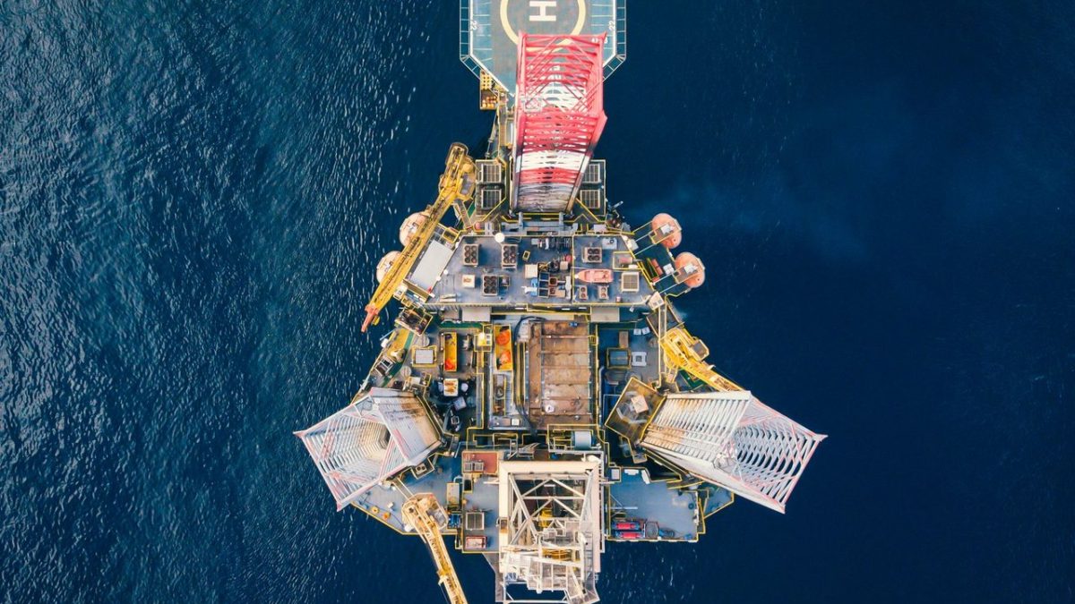 Vista aérea de uma plataforma de petróleo offshore cercada pelo mar azul.