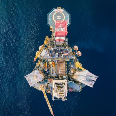 Vista aérea de uma plataforma de petróleo offshore cercada pelo mar azul.