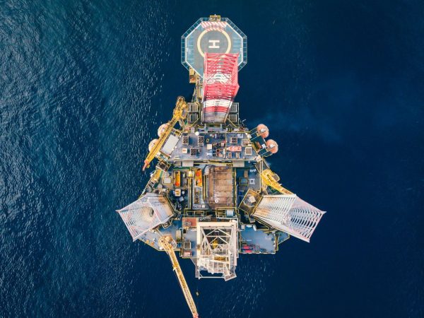 Vista aérea de uma plataforma de petróleo offshore cercada pelo mar azul.