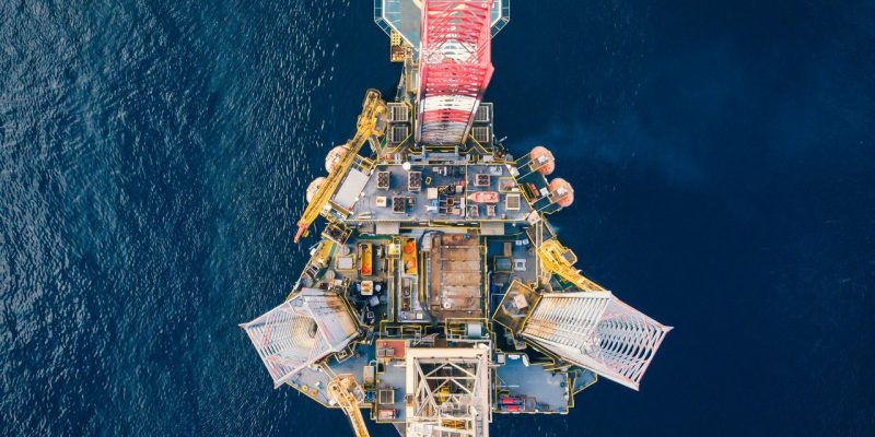 Vista aérea de uma plataforma de petróleo offshore cercada pelo mar azul.