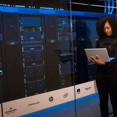Profissional monitora servidores com um laptop em uma moderna sala de equipamentos.