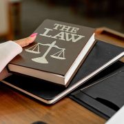 Livro intitulado “The Law” sobre uma mesa de madeira, ao lado de uma balança da Justiça.