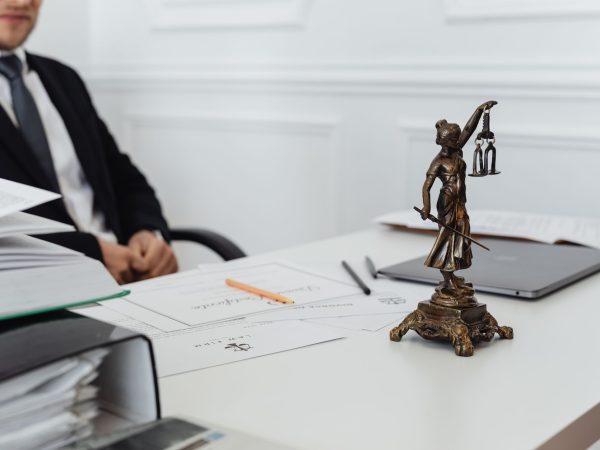 Mesa de trabalho jurídico com documentos, laptop e uma estátua da Justiça.
