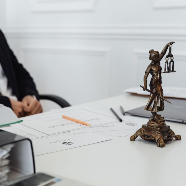 Mesa de trabalho jurídico com documentos, laptop e uma estátua da Justiça.