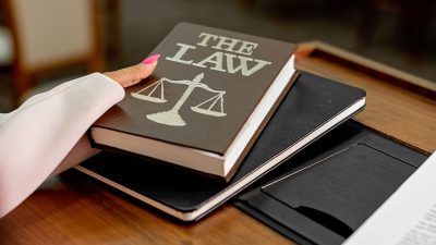 Livro intitulado “The Law” sobre uma mesa de madeira, ao lado de uma balança da Justiça.