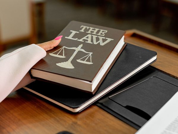 Livro intitulado “The Law” sobre uma mesa de madeira, ao lado de uma balança da Justiça.