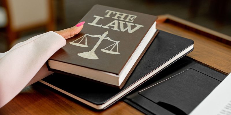 Livro intitulado “The Law” sobre uma mesa de madeira, ao lado de uma balança da Justiça.
